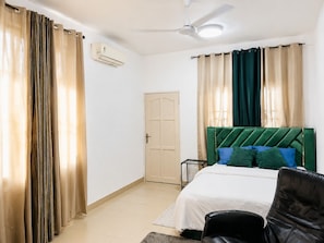 Een slaapkamer met een bed, een stoel, een deur en gordijnen.