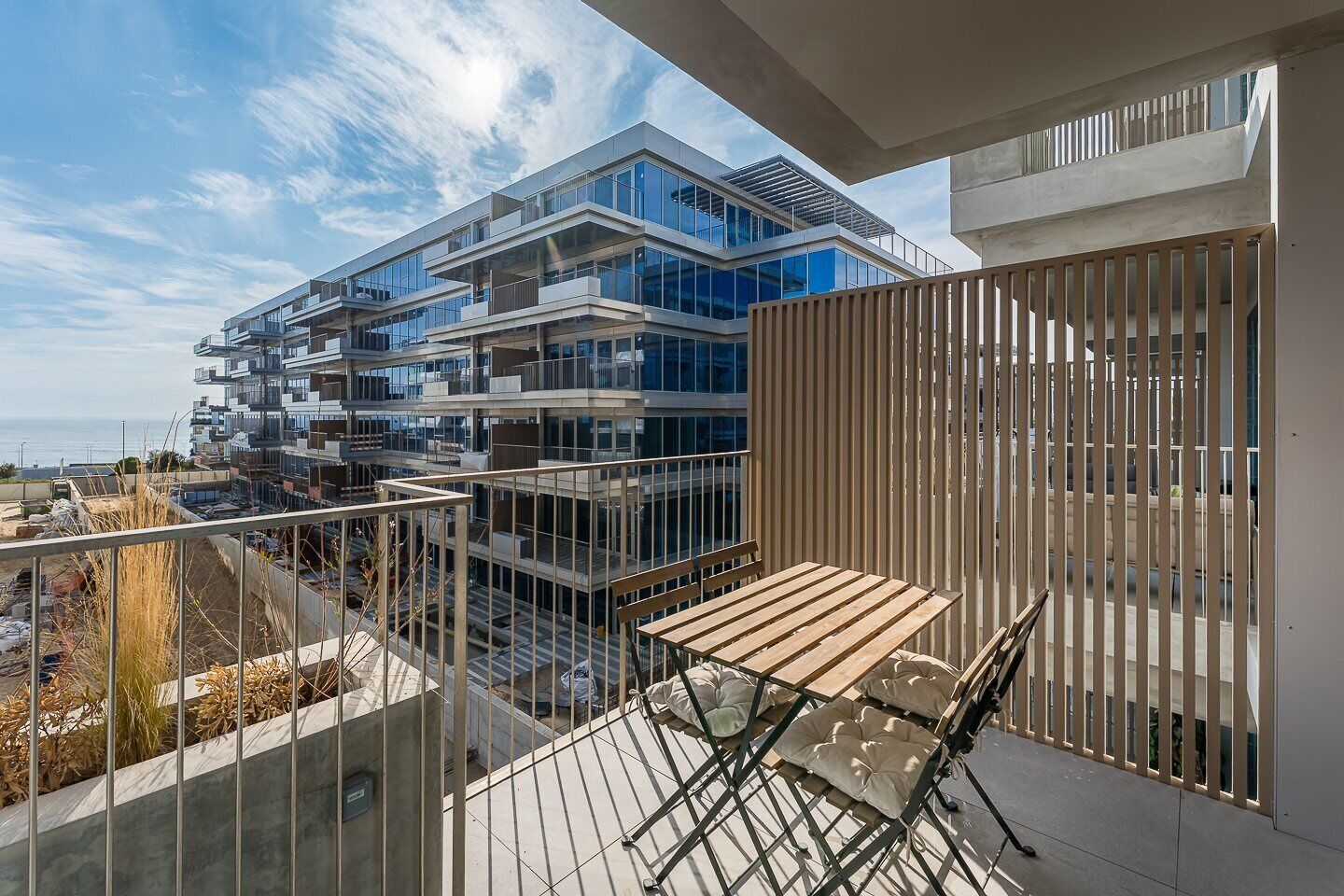 A modern apartment with a balcony, a view of a cityscape, and a clear sky.