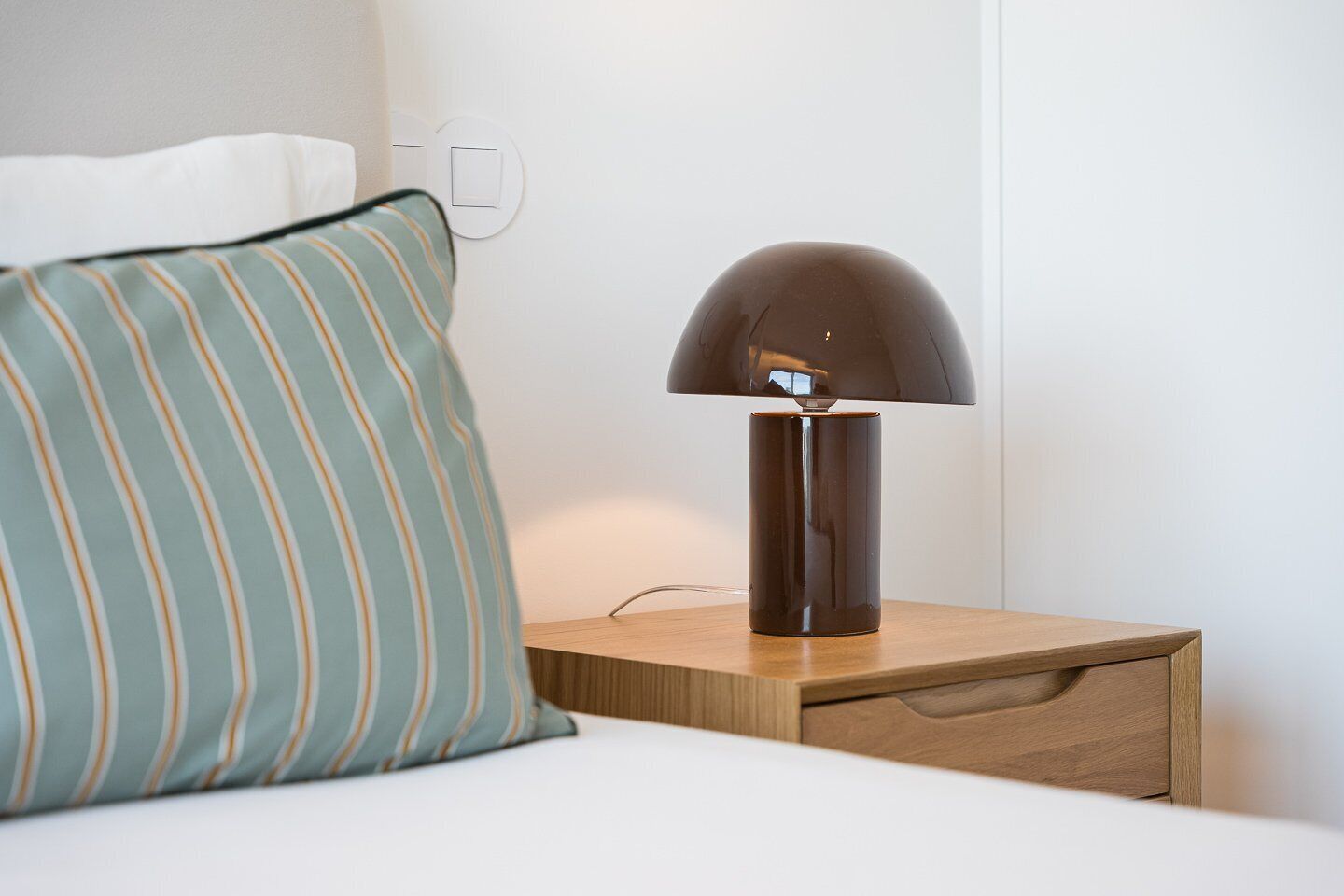 Ein Nachttisch mit Lampe, Kissen und einer Steckdose an der Wand.