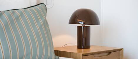 Ein Nachttisch mit Lampe, Kissen und einer Steckdose an der Wand.