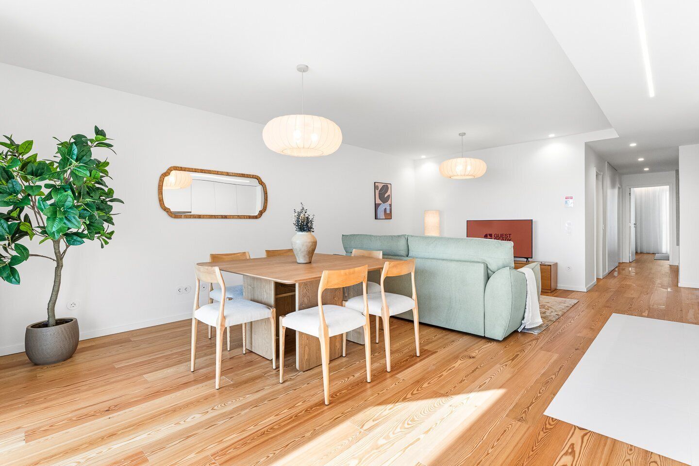 A modern living room with a dining area, a sofa, a potted plant, and a mirror on the wall.