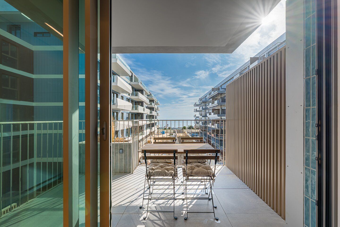 A balcony with a table and chairs, overlooking a residential area with multiple buildings.