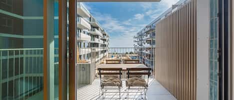 A balcony with a table and chairs, overlooking a residential area with multiple buildings.
