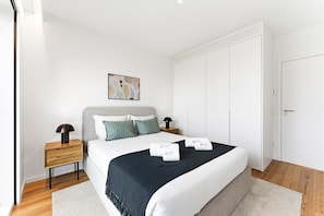 Een moderne slaapkamer met een bed, nachtkastjes, een schilderij en een kledingkast.