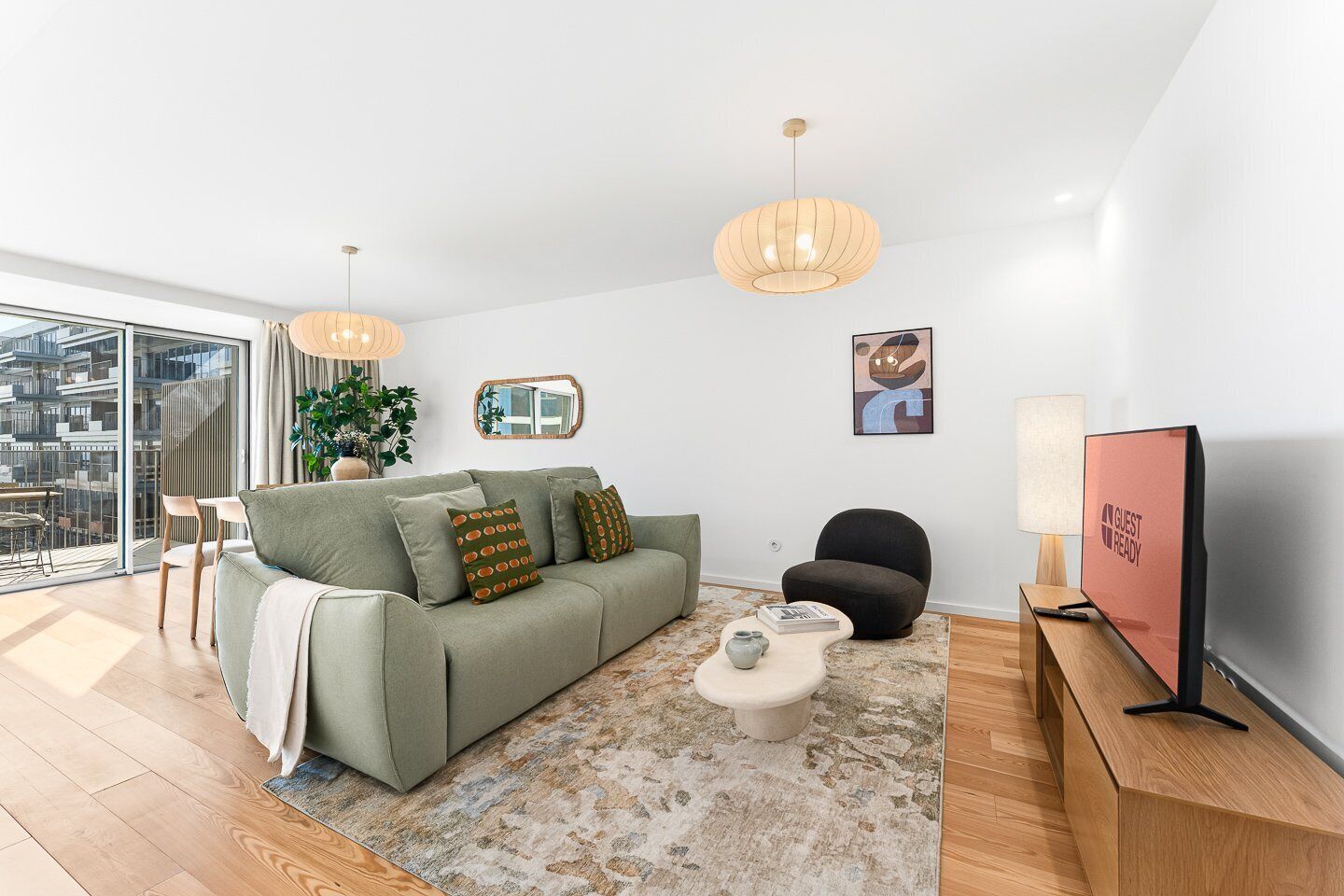 A modern living room with a sofa, a coffee table, a chair, a TV, and a large window offering a city view.