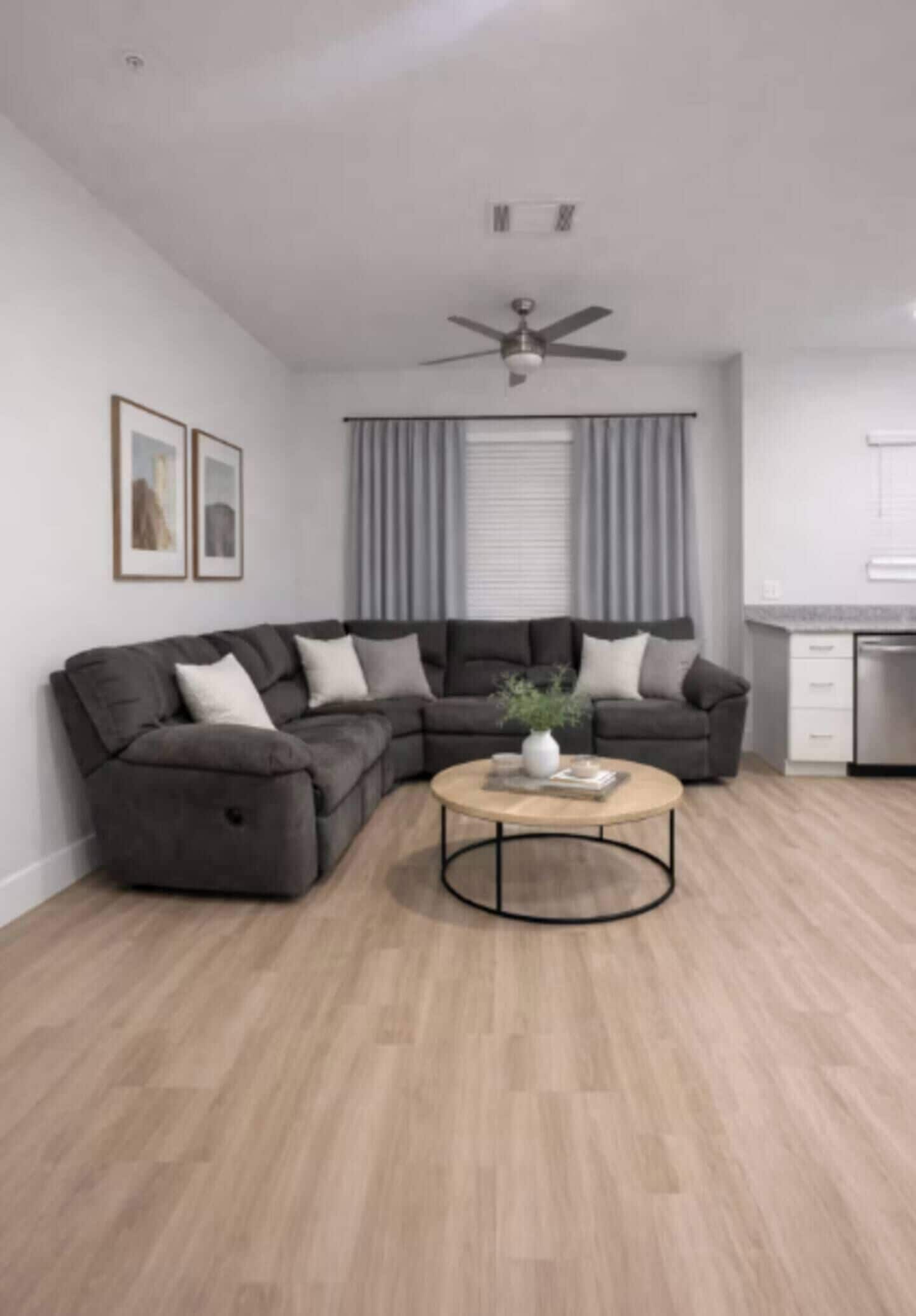 A modern living room with a sectional sofa, a round coffee table, and a ceiling fan.