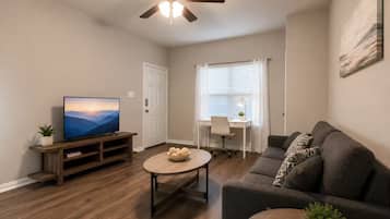 A living room with a television, a coffee table, a sofa, a ceiling fan, and a window with blinds.