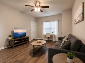 Ein Wohnzimmer mit Fernseher, Couchtisch, Sofa, Deckenventilator und einem Fenster mit Jalousien.