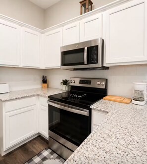 A kitchen with white cabinets, a stainless steel stove, a microwave, and a coffee maker.