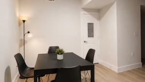 A dining area with a table, four chairs, a small potted plant, and a floor lamp.