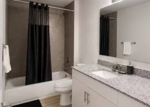 A modern bathroom with a bathtub, toilet, and a large mirror.