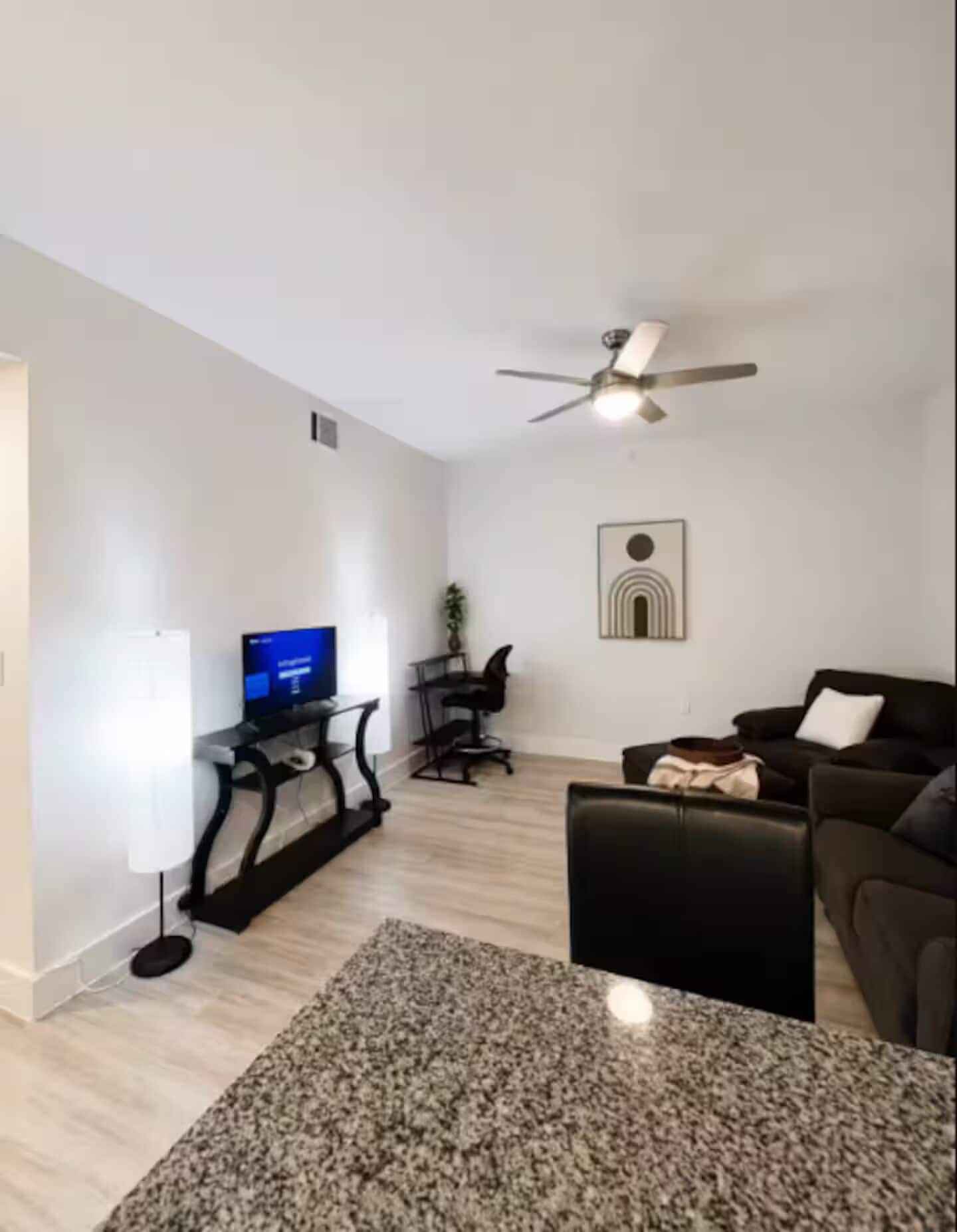 A living room with a flat-screen TV, a ceiling fan, a coffee table, and a sofa.