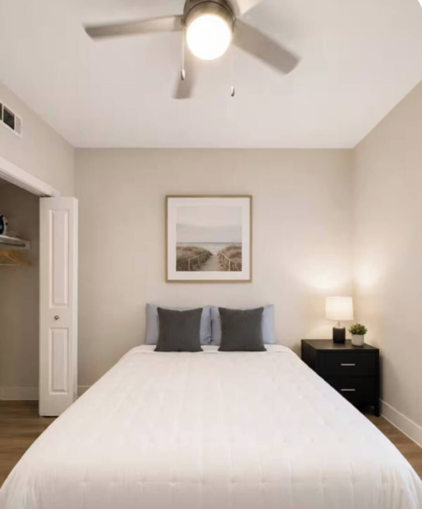 A bedroom with a bed, a nightstand, a ceiling fan, and a framed picture on the wall.