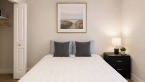 A bedroom with a bed, a nightstand, a ceiling fan, and a framed picture on the wall.