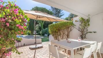 Une terrasse extérieure avec une table et des chaises, entourée de verdure et d’un mur blanc.