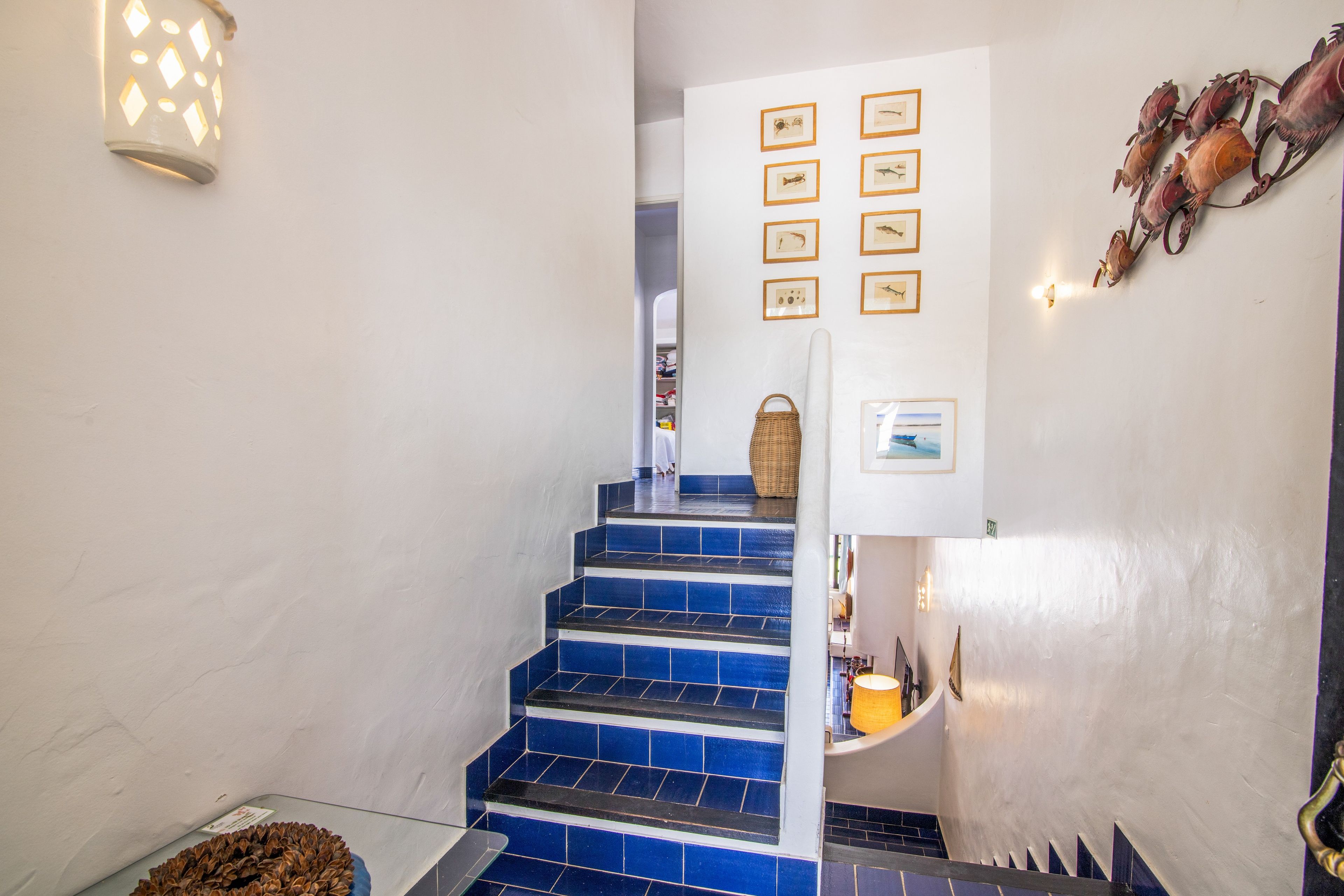 Un escalier recouvert de carreaux bleus mène à une pièce dont les murs sont ornés de tableaux encadrés.