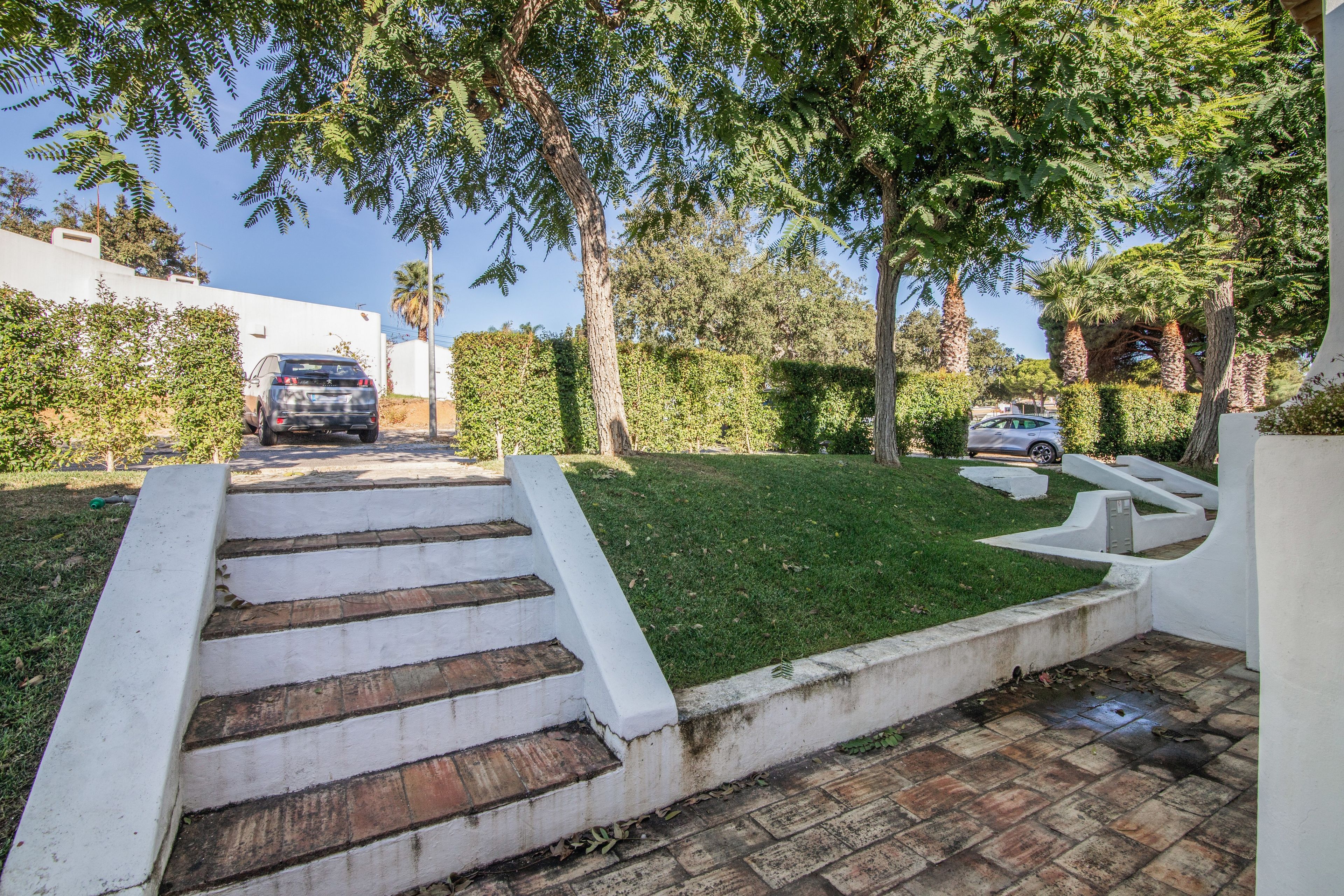 A residential driveway with a set of stairs leading to a garage, surrounded by lush greenery and trees.