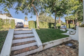 Un camino de entrada residencial con una escalera que conduce a un garaje, rodeado de exuberante follaje y árboles.