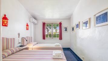 Une chambre d’hôtel avec deux lits, une fenêtre avec des rideaux, un climatiseur fixé au mur et des œuvres d’art encadrées.