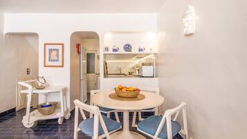 Un coin repas avec une table ronde, des chaises et un saladier rempli de fruits.
