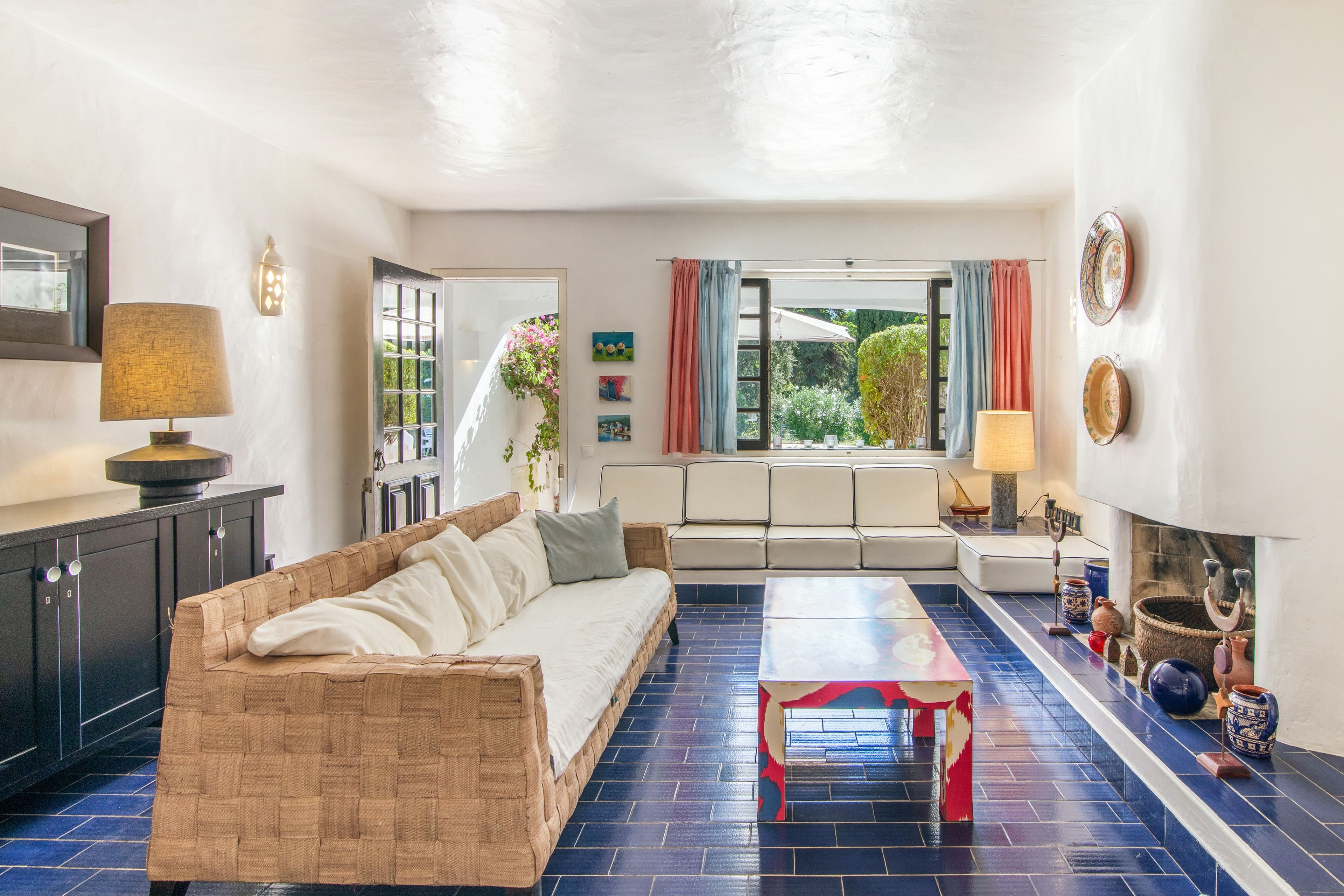 Un salon comprenant un canapé, une table basse et une cheminée. Des objets décoratifs sont disposés sur la cheminée, et les fenêtres offrent une vue sur l’extérieur.