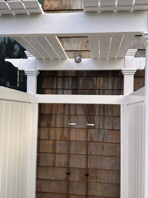 A white pergola structure with a built-in light fixture above a wooden door with two locks. - Luxury Coastal Retreat w/Heated Pool (Mantoloking)