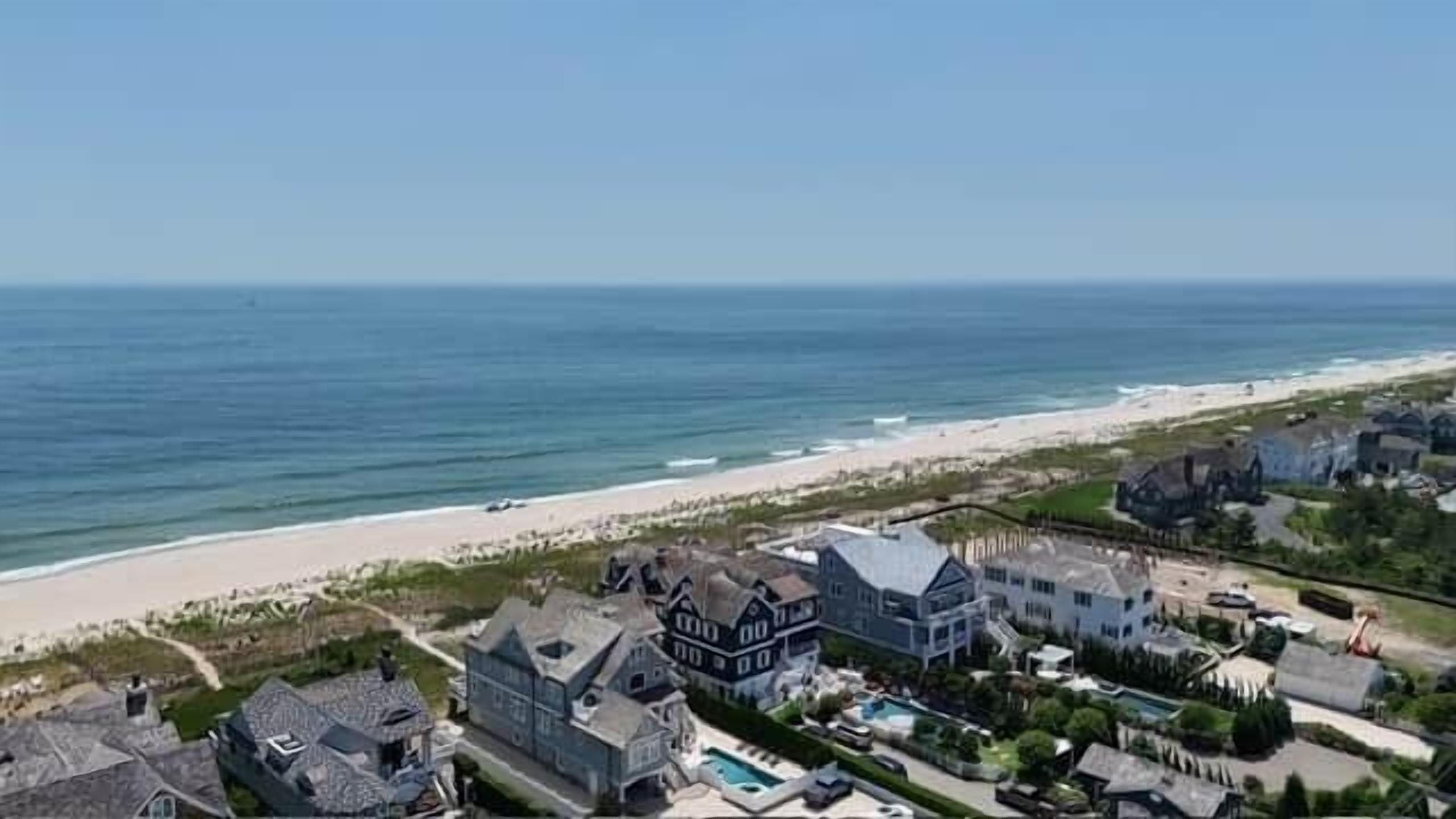 A coastal residential area with houses, a beach, and a clear sky.