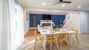 Un comedor con una mesa blanca y sillas de madera, una chimenea y una escalera que sube a otro nivel.