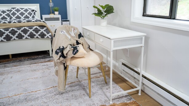 Un dormitorio con cama, escritorio, silla, planta y ventana.