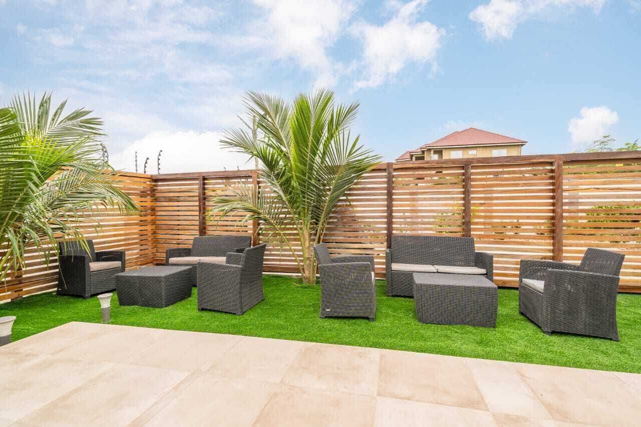 An outdoor patio area with wicker furniture, artificial grass, and a wooden fence.
