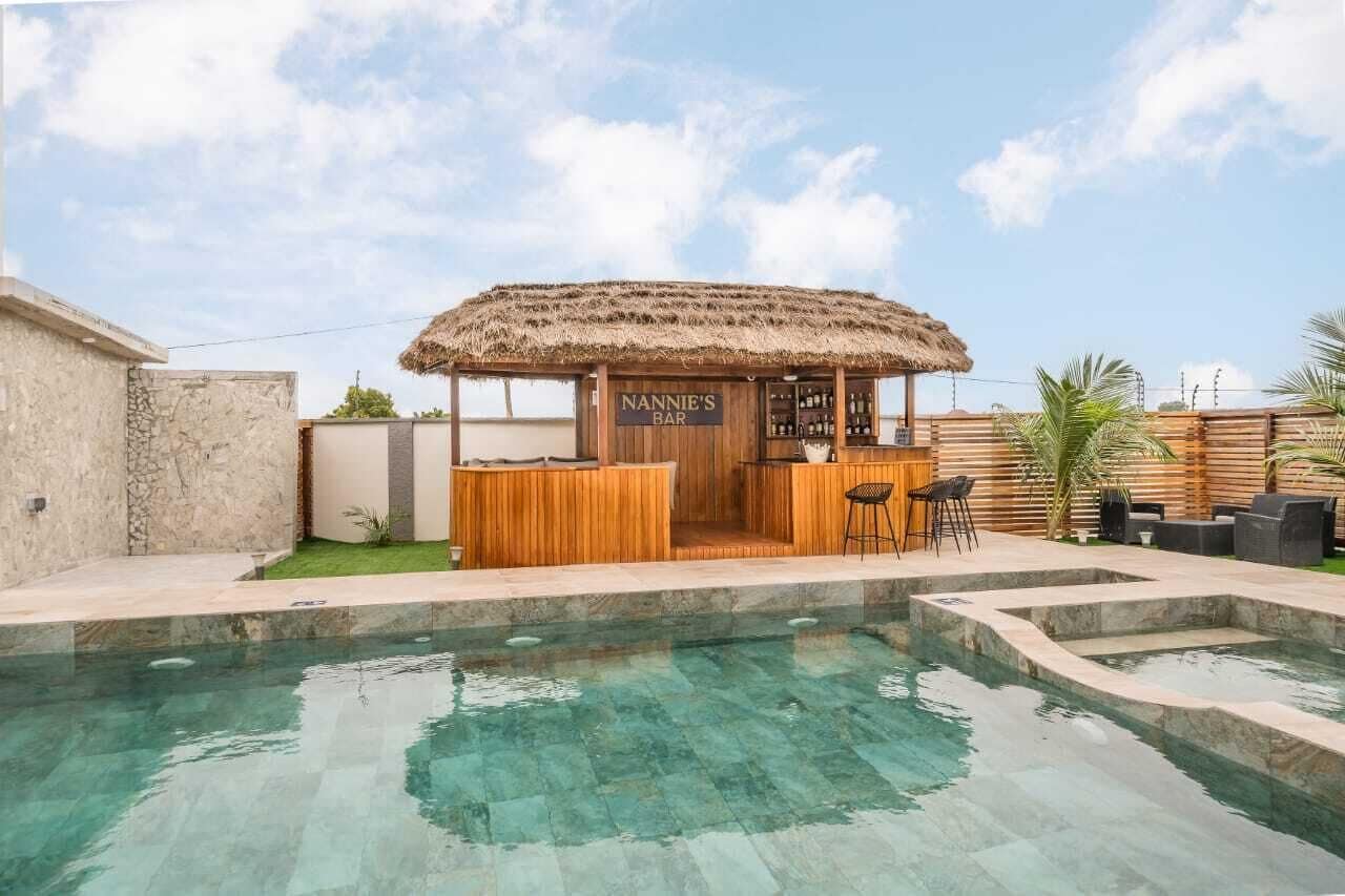 A poolside bar with a thatched roof, wooden seating, and a sign reading 'NANNIE'S BAR'.