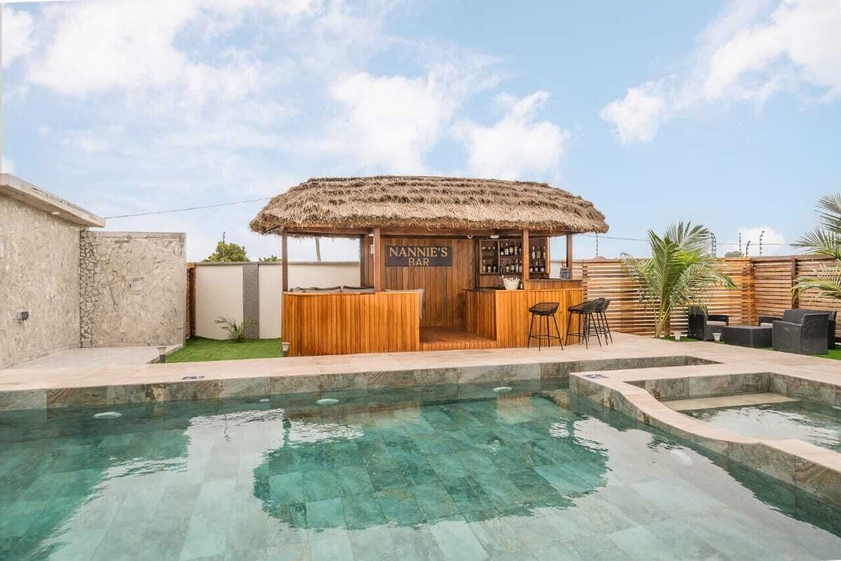 Un bar situé au bord de la piscine, doté d’un toit de chaume, de sièges en bois et d’une enseigne indiquant « BAR DE NANNIE ».