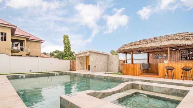 A swimming pool with a hot tub, a bar area, and a small building with a door. - Crown Luxury Apartments  (Kokrobite)