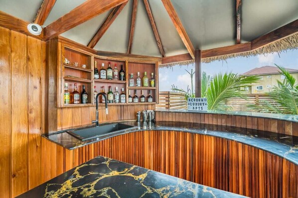 A bar area with wooden shelves and a curved counter, overlooking a residential area. - Crown Luxury Apartments  (Kokrobite)