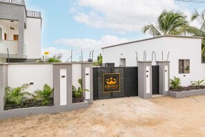 Une entrée sécurisée, agrémentée d’un panneau « Crown », une façade de bâtiment moderne et un espace paysager avec des plantes tropicales.