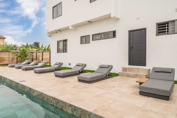 A modern building with a poolside area featuring multiple lounge chairs.