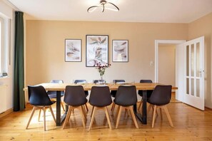 A dining area with a long wooden table, six chairs, and three framed artworks on the wall. - Ferienwohnung mit Terrasse (Würzburg)
