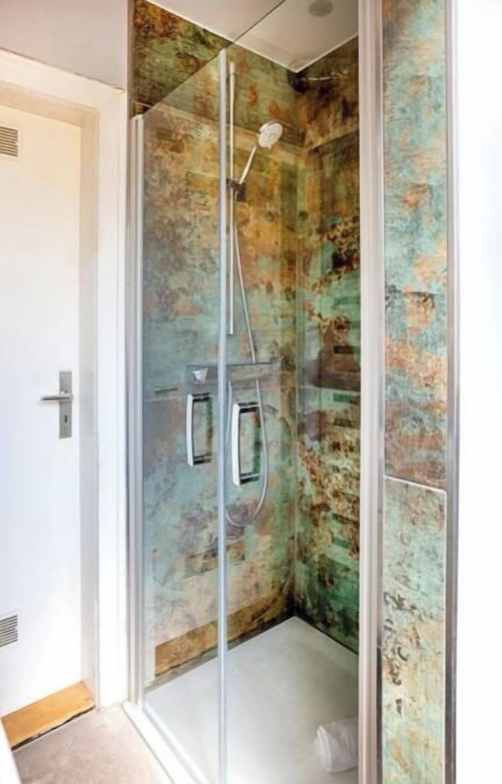 A glass-enclosed shower with a rustic wall design.