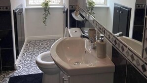 Een badkamer met toilet, wastafel en spiegel. Er is een raam boven het toilet en een plant die aan de muur hangt.