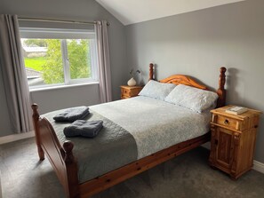 A neatly made bed with a wooden headboard and footboard, a bedside table with a book, and a window with curtains.