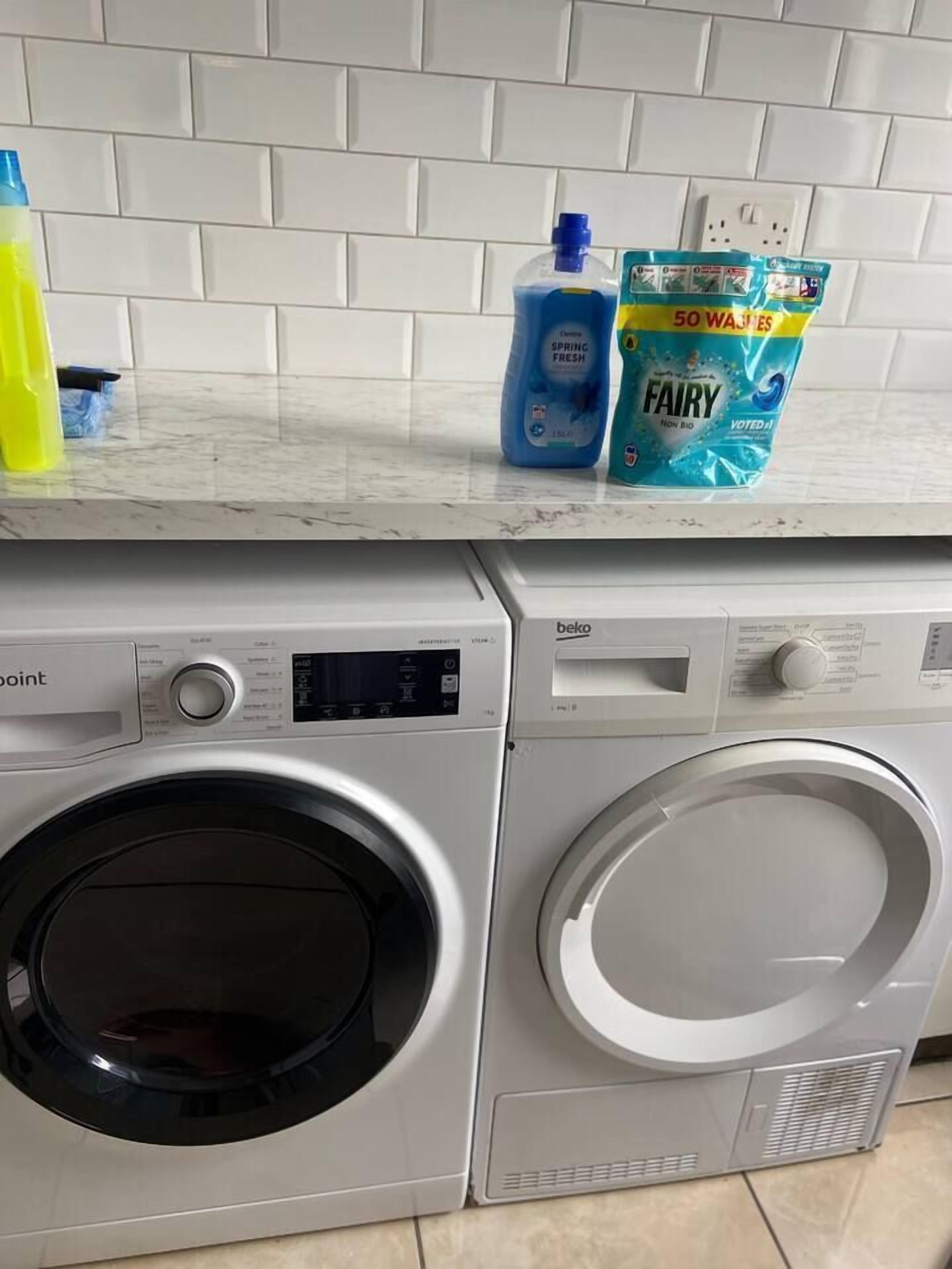 A front-loading washing machine and dryer in a kitchen area with a tiled backsplash.
