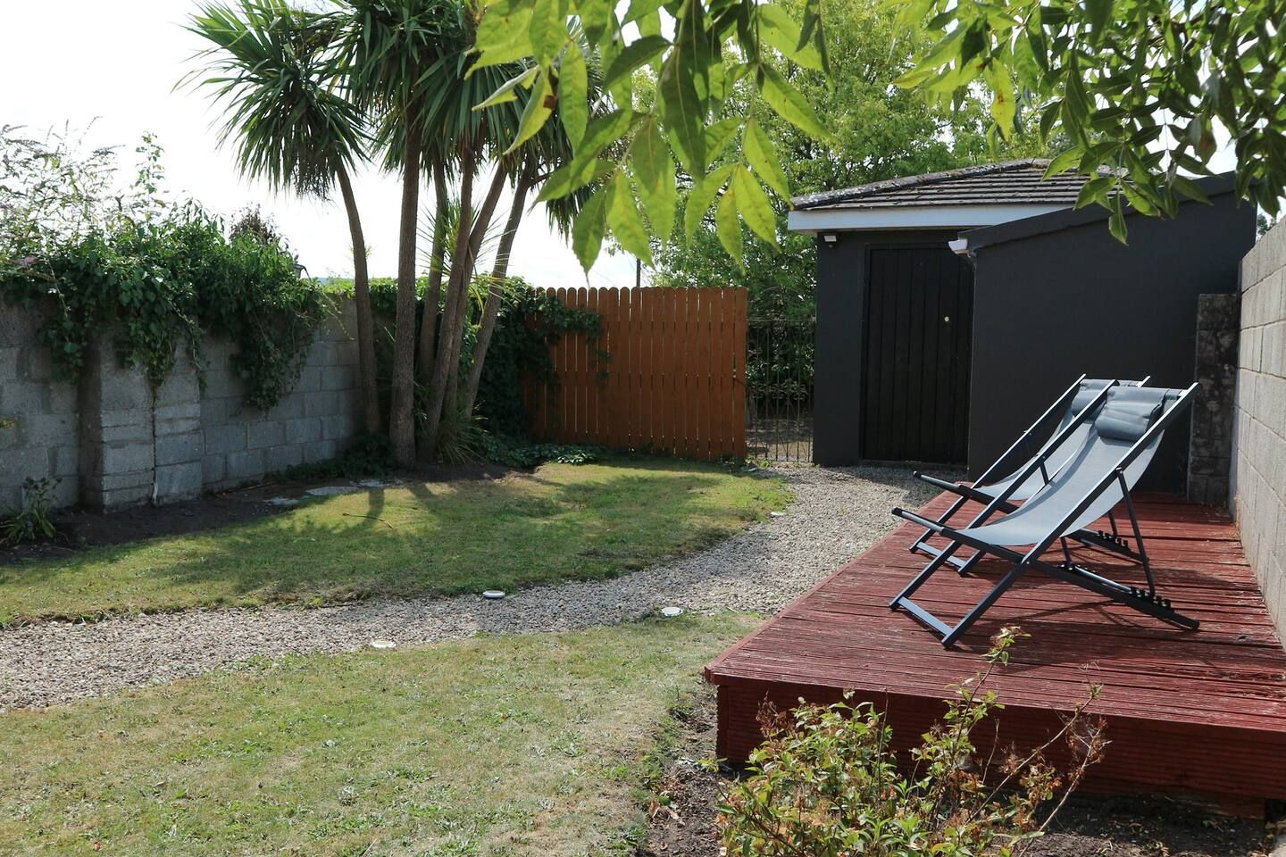 Een achtertuin met een kleine schuur, een houten terras en twee comfortabele stoelen.