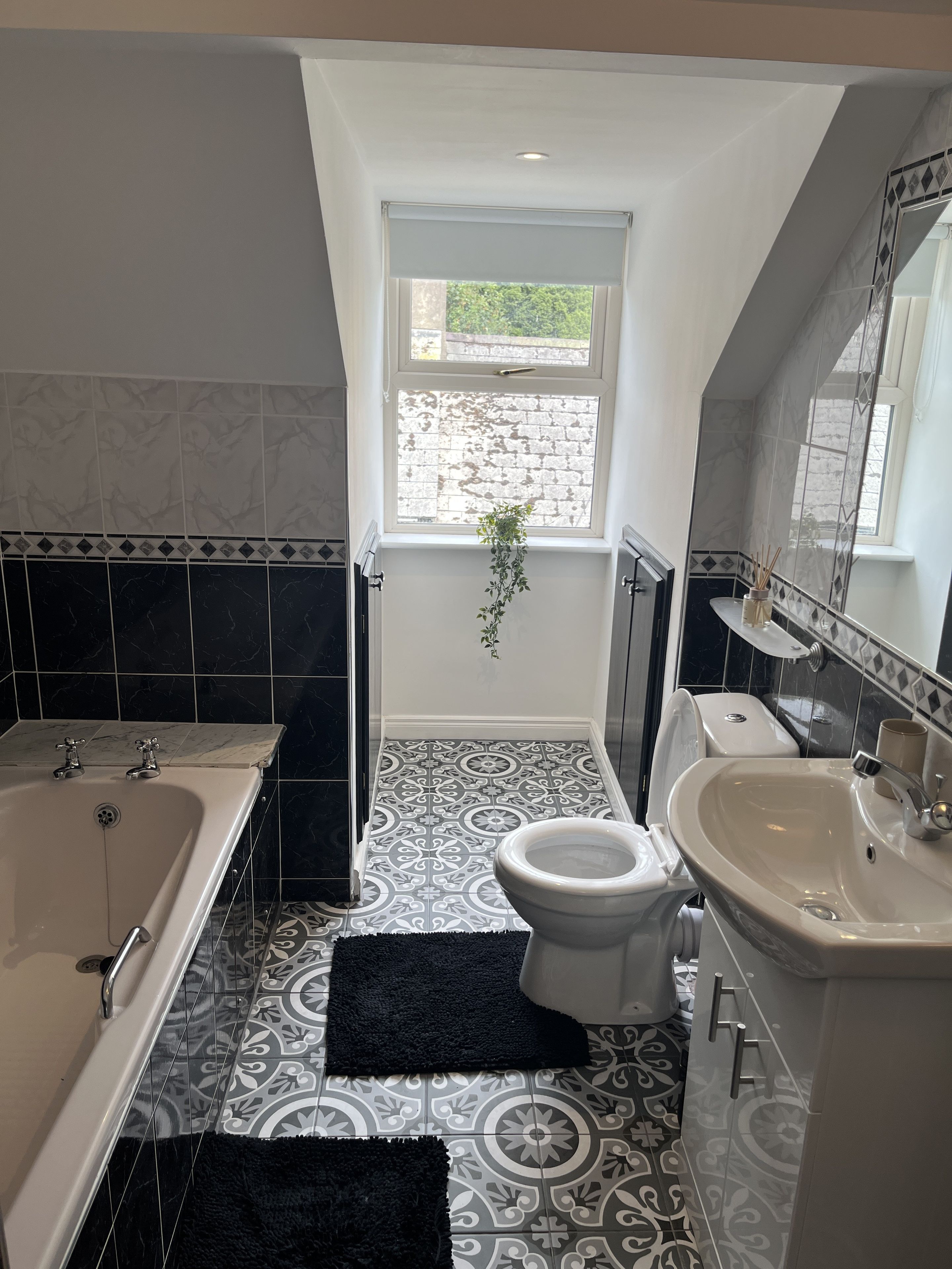 Une salle de bain équipée d’une baignoire, de toilettes et d’un lavabo, avec des carreaux décoratifs et une fenêtre offrant une vue agréable.