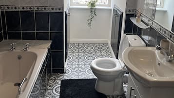 Une salle de bain équipée d’une baignoire, de toilettes et d’un lavabo, avec des carreaux décoratifs et une fenêtre offrant une vue agréable.