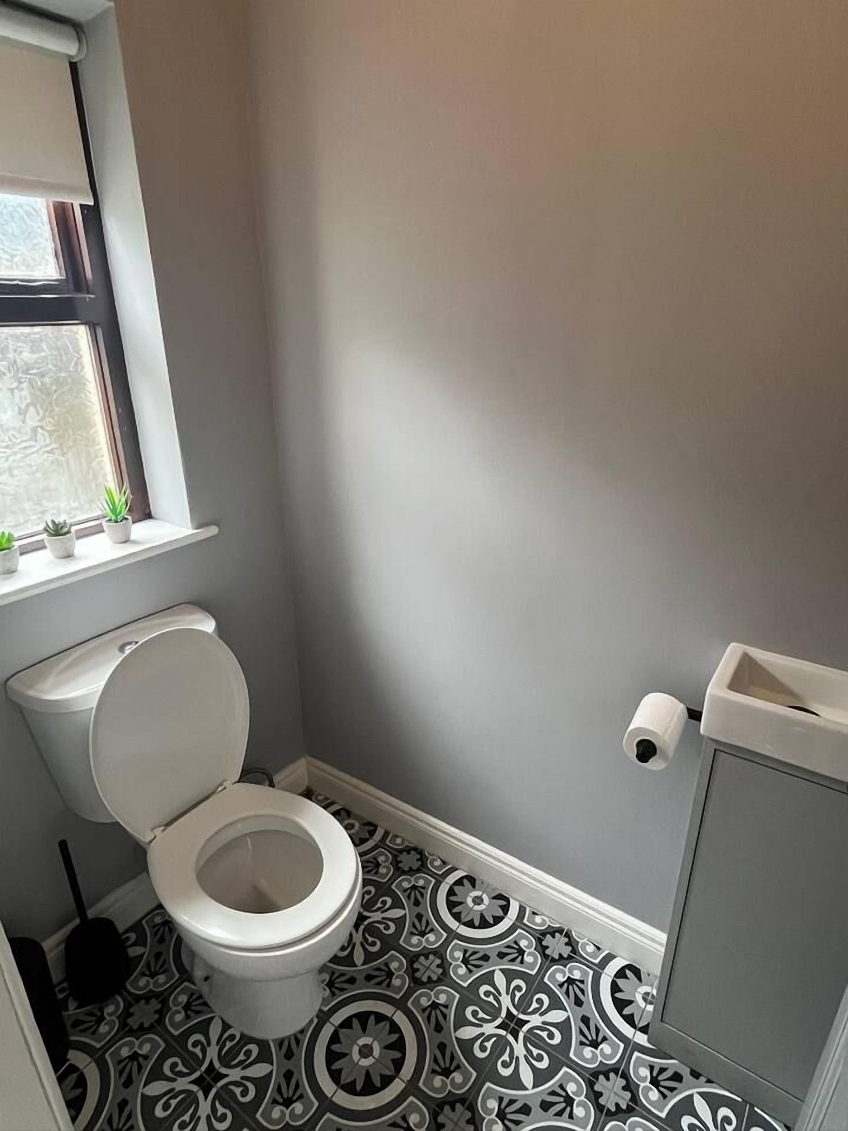 Une petite salle de bain avec des toilettes, une fenêtre ornée de plantes et des carreaux de sol à motifs.