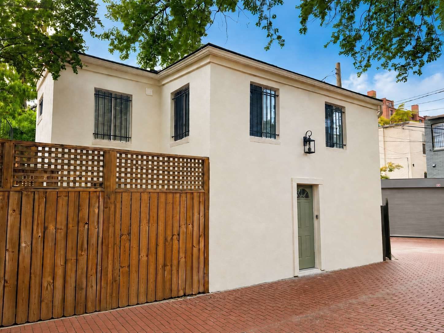 Un bâtiment à deux étages, avec une clôture en bois, une porte verte et un chemin pavé de briques.