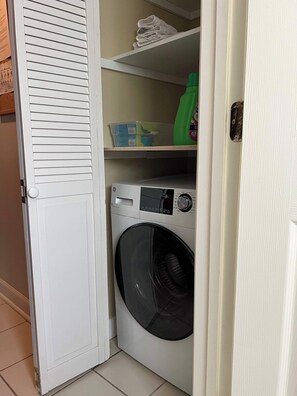 A laundry room with a front-loading washing machine, shelves with folded towels, and a green bottle of detergent. - Dupont Circle Carriage House! With laundry/kitchen/AC (Washington)