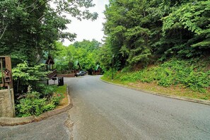 A road curving through a wooded area with a stone structure and a green-roofed building. - Mountain View Retreat 🏔️ Private Hot Tub, Arcade Room, Steps to Pigeon Forge Fun (Pigeon Forge)