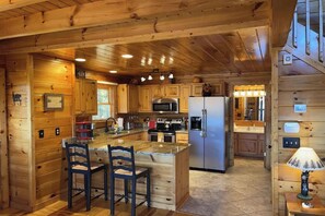 A wooden cabin kitchen with a central island, bar stools, a refrigerator, and a microwave. - Mountain View Retreat 🏔️ Private Hot Tub, Arcade Room, Steps to Pigeon Forge Fun (Pigeon Forge)