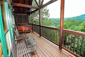 A wooden deck with outdoor furniture, a view of a forested landscape, and a building with green trim. - Mountain View Retreat 🏔️ Private Hot Tub, Arcade Room, Steps to Pigeon Forge Fun (Pigeon Forge)